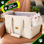 A cream-colored pet carrier tote bag with a fluffy white cat sitting inside, placed on a brown leather chair. The bag has dual handles, a zippered top, and a small brown brand patch on the front pocket.