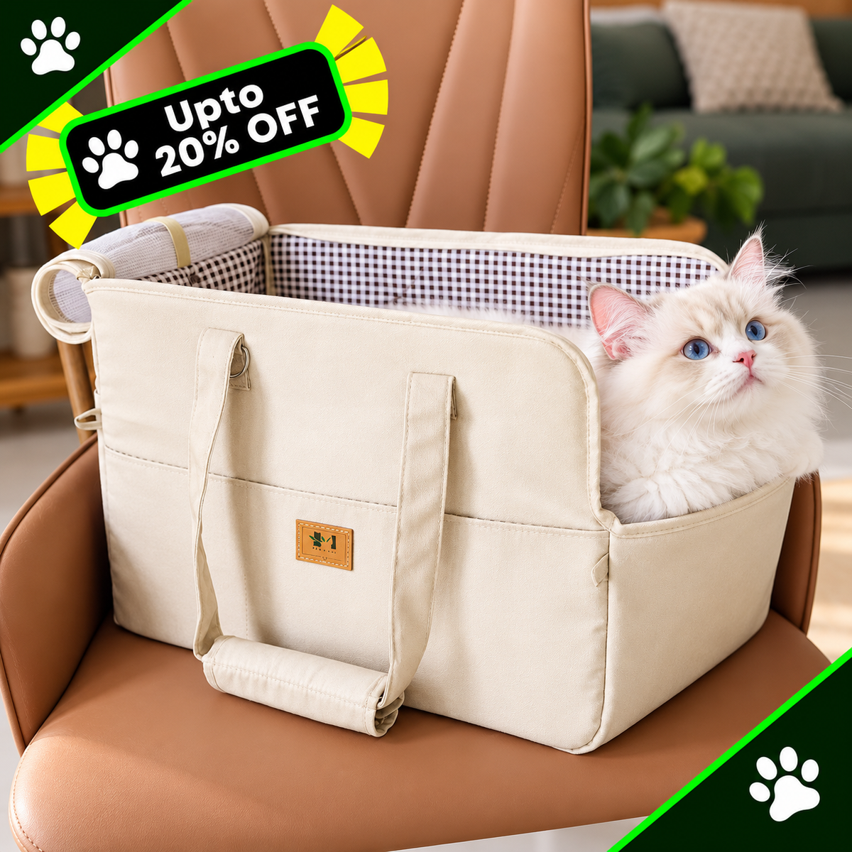 A cream-colored pet carrier tote bag with a fluffy white cat sitting inside, placed on a brown leather chair. The bag has dual handles, a zippered top, and a small brown brand patch on the front pocket.