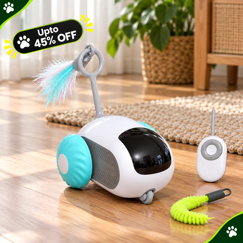 A small white and turquoise robotic cat toy with a black face window, a feather wand, and a separate remote controller on a wooden floor. A green coiled toy is also placed nearby.