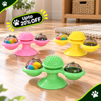 Three pet massage toys in pink, yellow, and green are arranged on a wooden floor. Each toy has a suction cup base, a central spiky massage dome, and two side cups containing colorful faux fur puffs under clear domes.